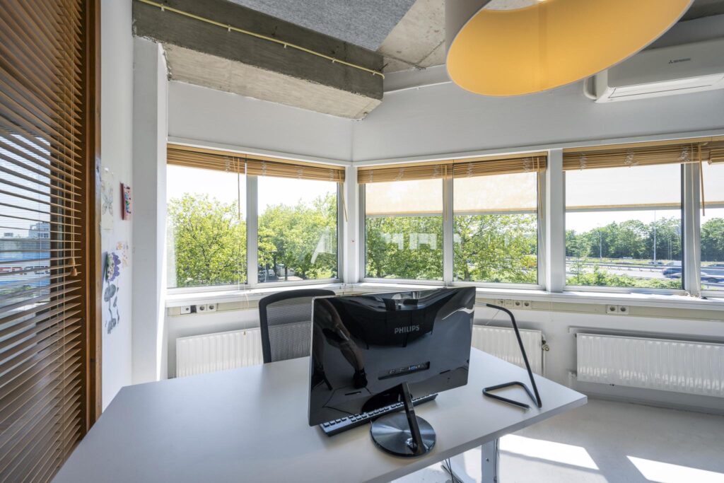 Modern en licht kantoor aan de Anthony Fokkerweg met een bureau, computerscherm en uitzicht op groen en snelweg.